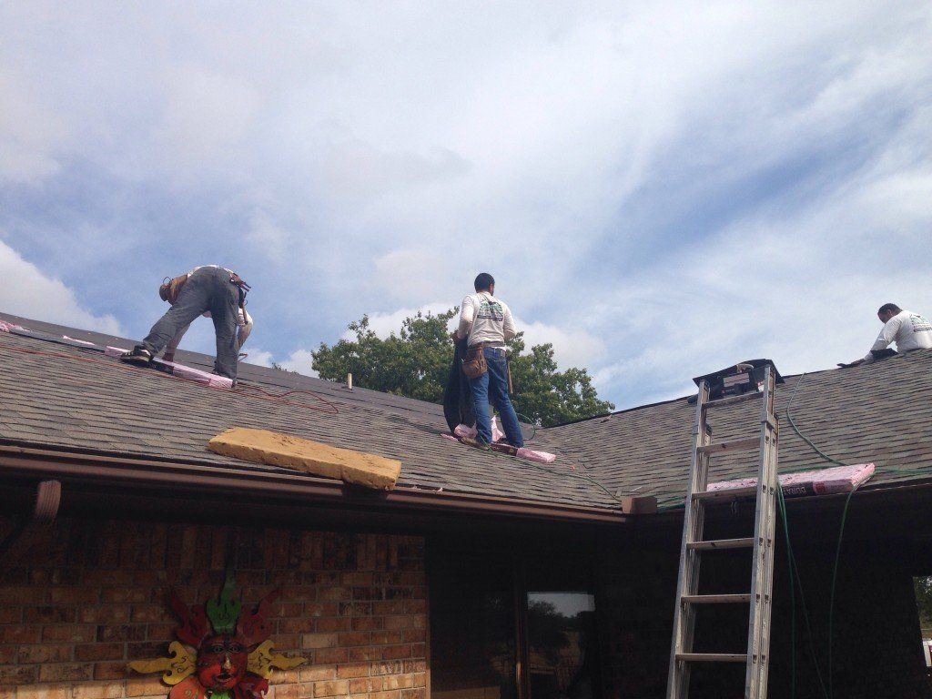 a group of men are working on a roof and one of them is wearing a shirt that says ' texas ' on it