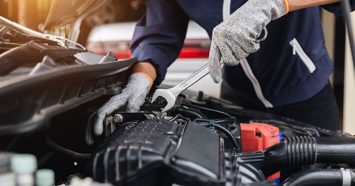 A mechanic in work gloves uses a wrench to perform maintenance on a car engine.