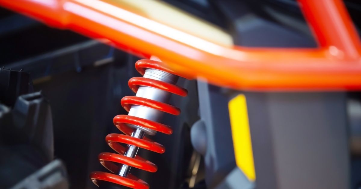 A close-up view of a red coil suspension spring and shock absorber on a vehicle with an orange roll cage.