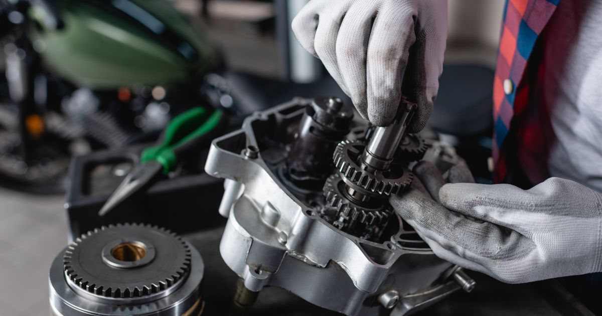 A mechanic in white gloves assembles metal motorcycle engine gears at a workbench.