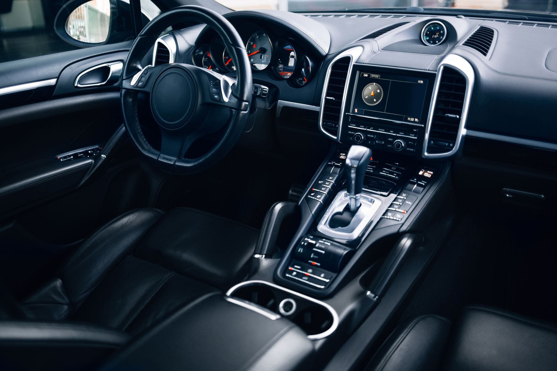 The interior of a black luxury car, showing the steering wheel, center console, leather seats, and infotainment system.