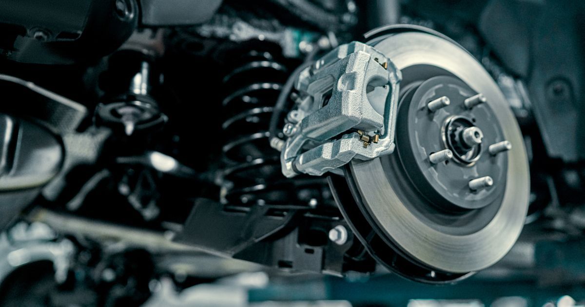 A close-up view of a car's rear suspension, disc brake rotor, and caliper mechanism with a dark coiled spring.