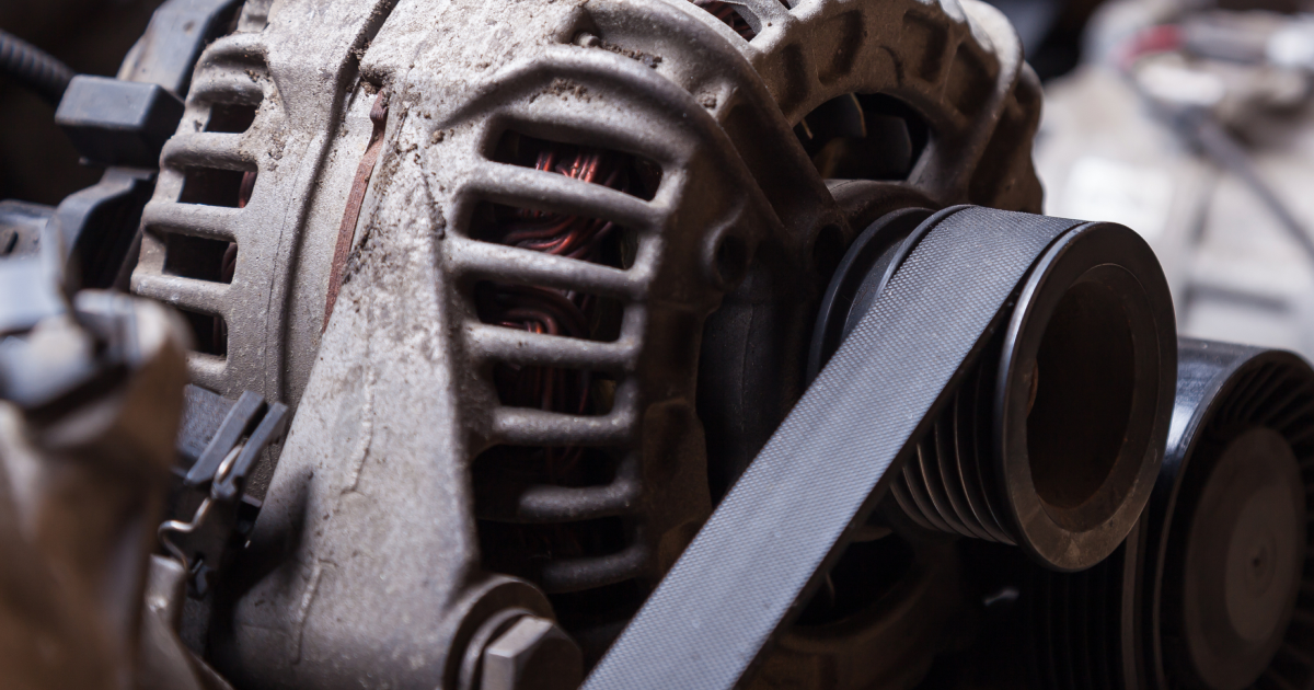 A car alternator with a ribbed serpentine belt wrapped around its pulley inside an engine bay.