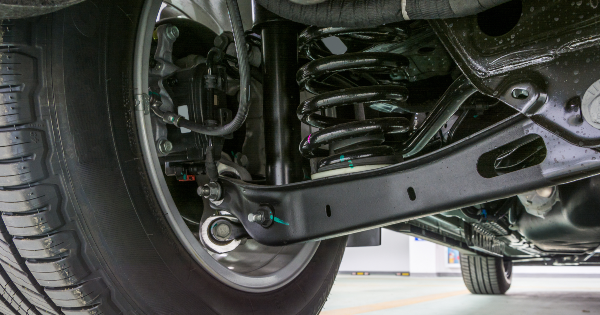 A close-up view of a car’s rear suspension system, featuring a black coil spring, control arm, and tire.