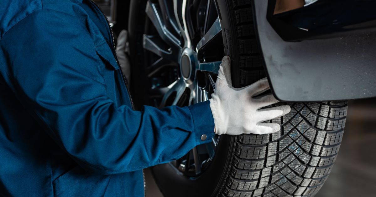 A mechanic in a blue uniform and white gloves installs a tire onto a car wheel.
