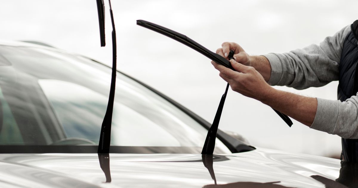 A person replaces a windshield wiper blade on a car.