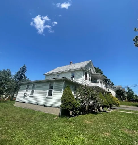 Two-story light green house with a small side addition, set on a green lawn under a blue sky.
