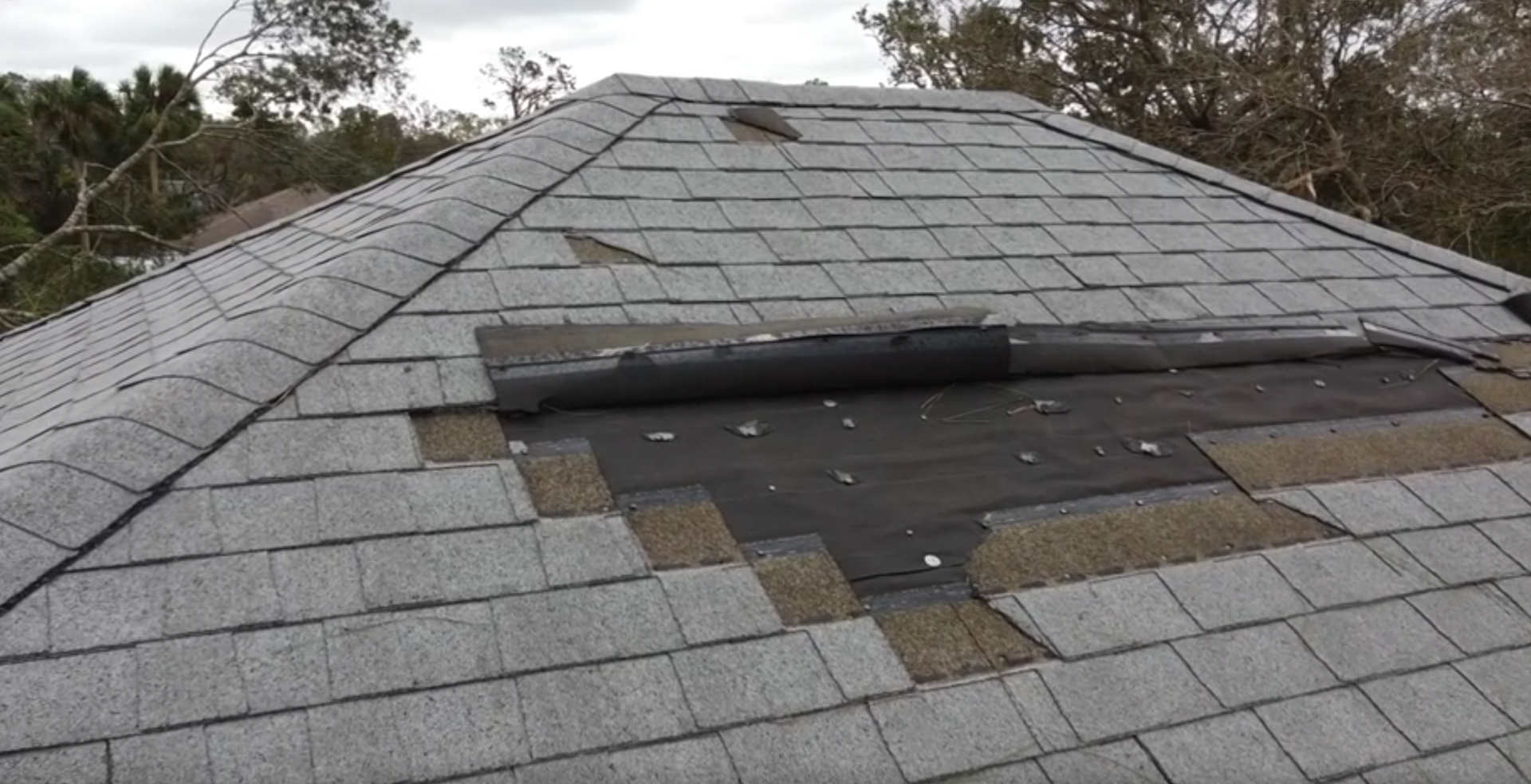 Workers repairing a damaged rooftop with scaffolding and blue tarps.
