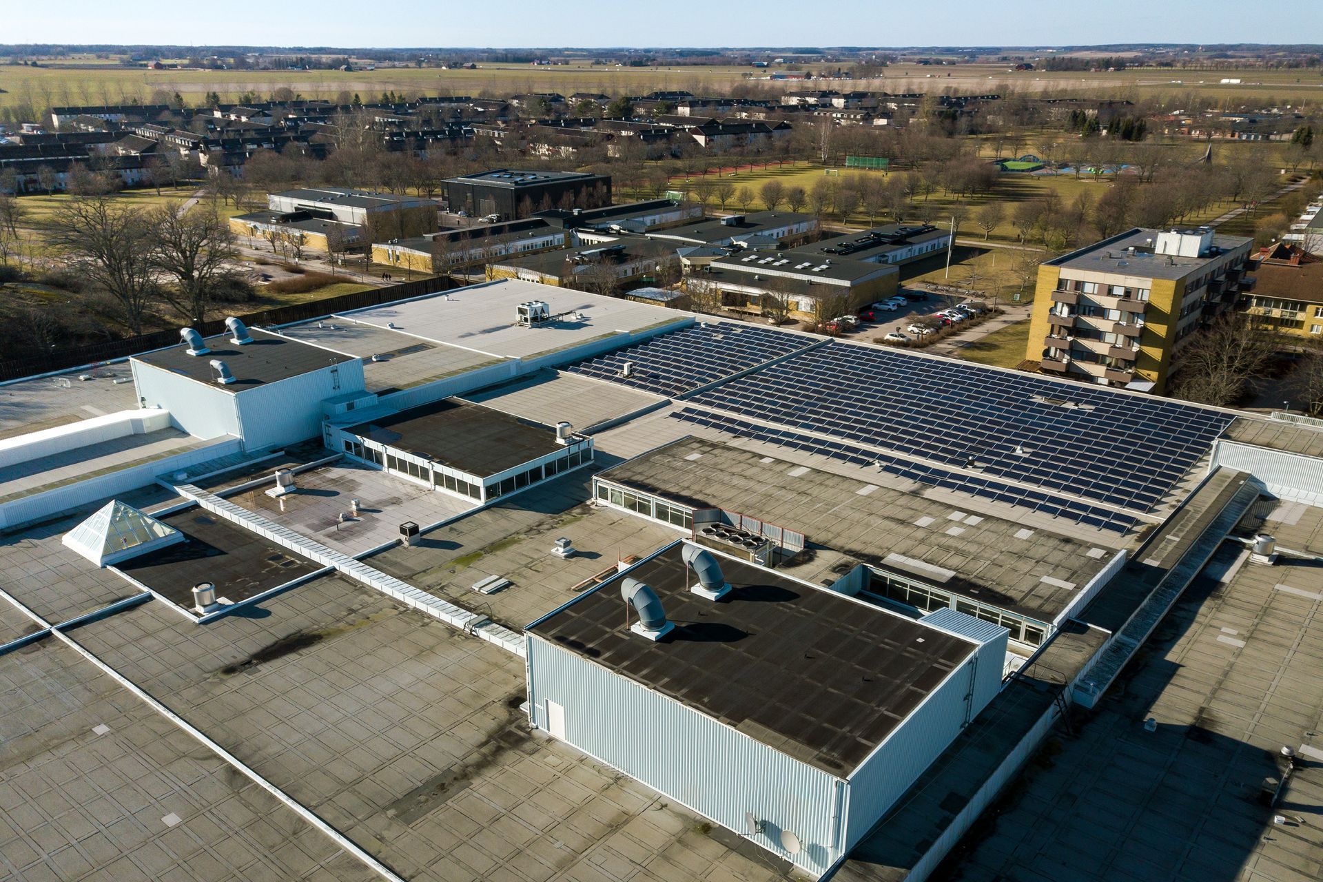 Aerial view of a building complex with a solar panel array on the roof and surrounding buildings.