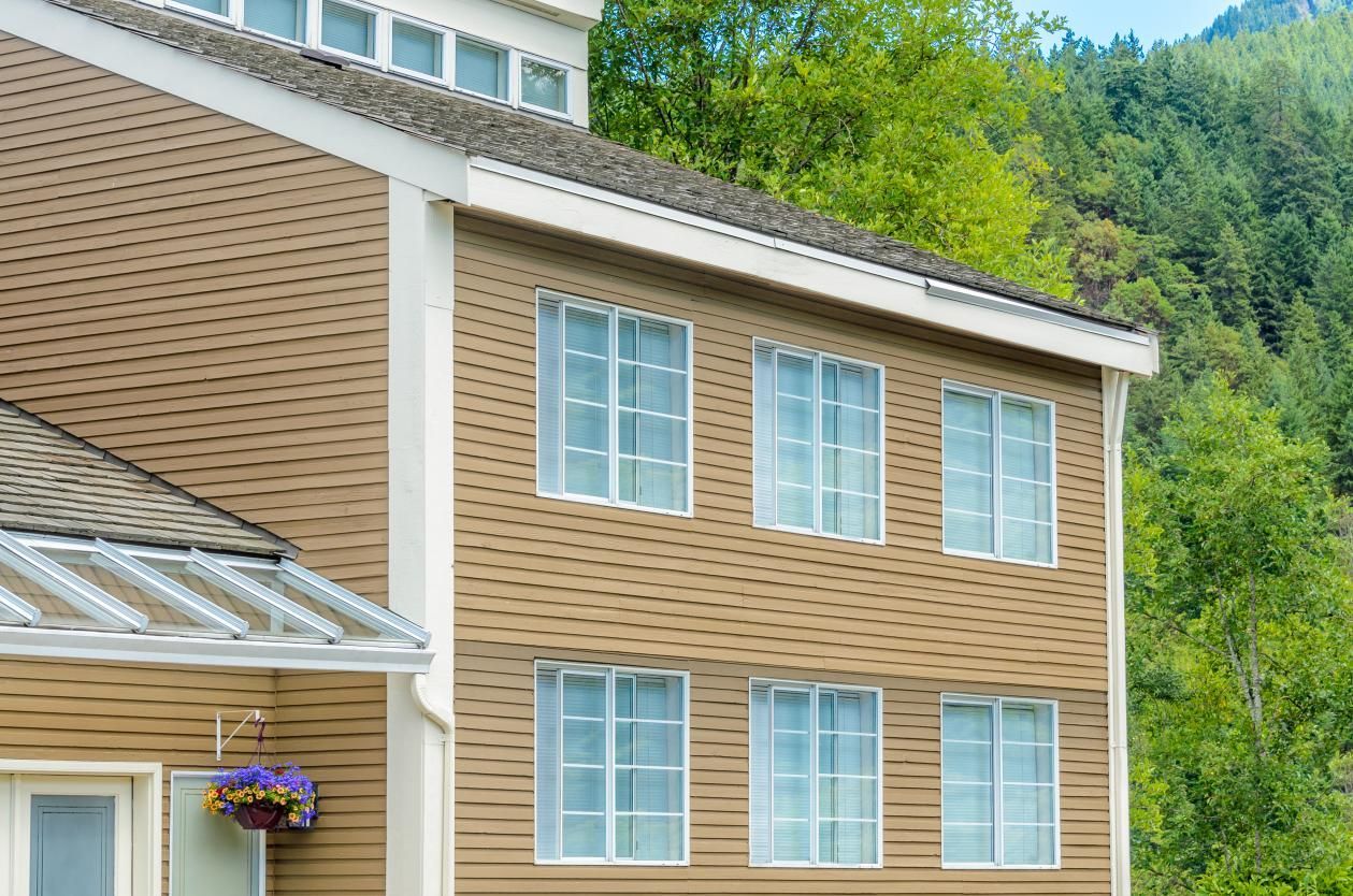 Two-story house with tan siding, multiple white-framed windows, and a mountain backdrop.