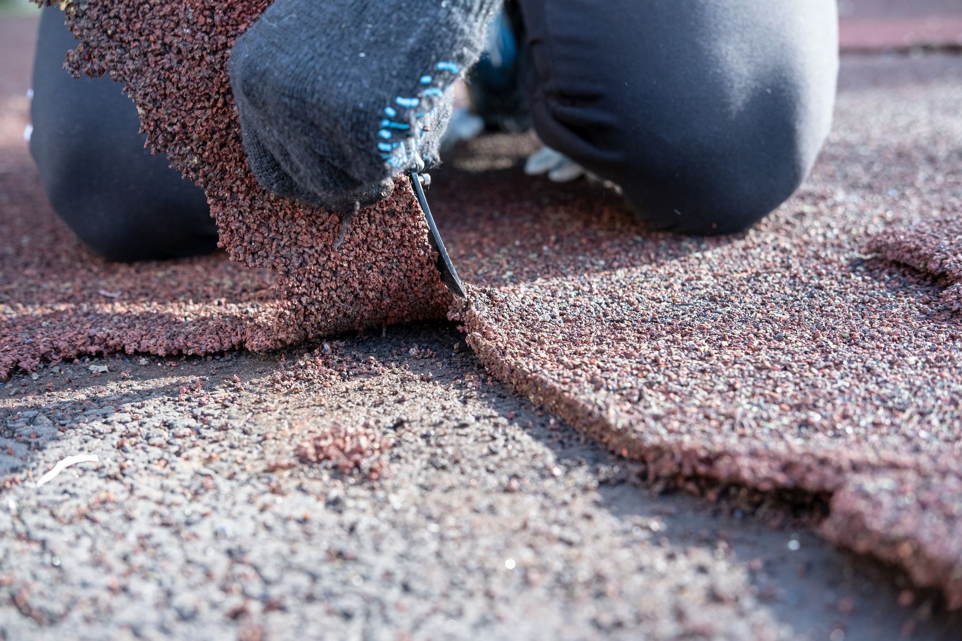 Person in gloves peeling up a section of red asphalt roofing shingles on a roof.