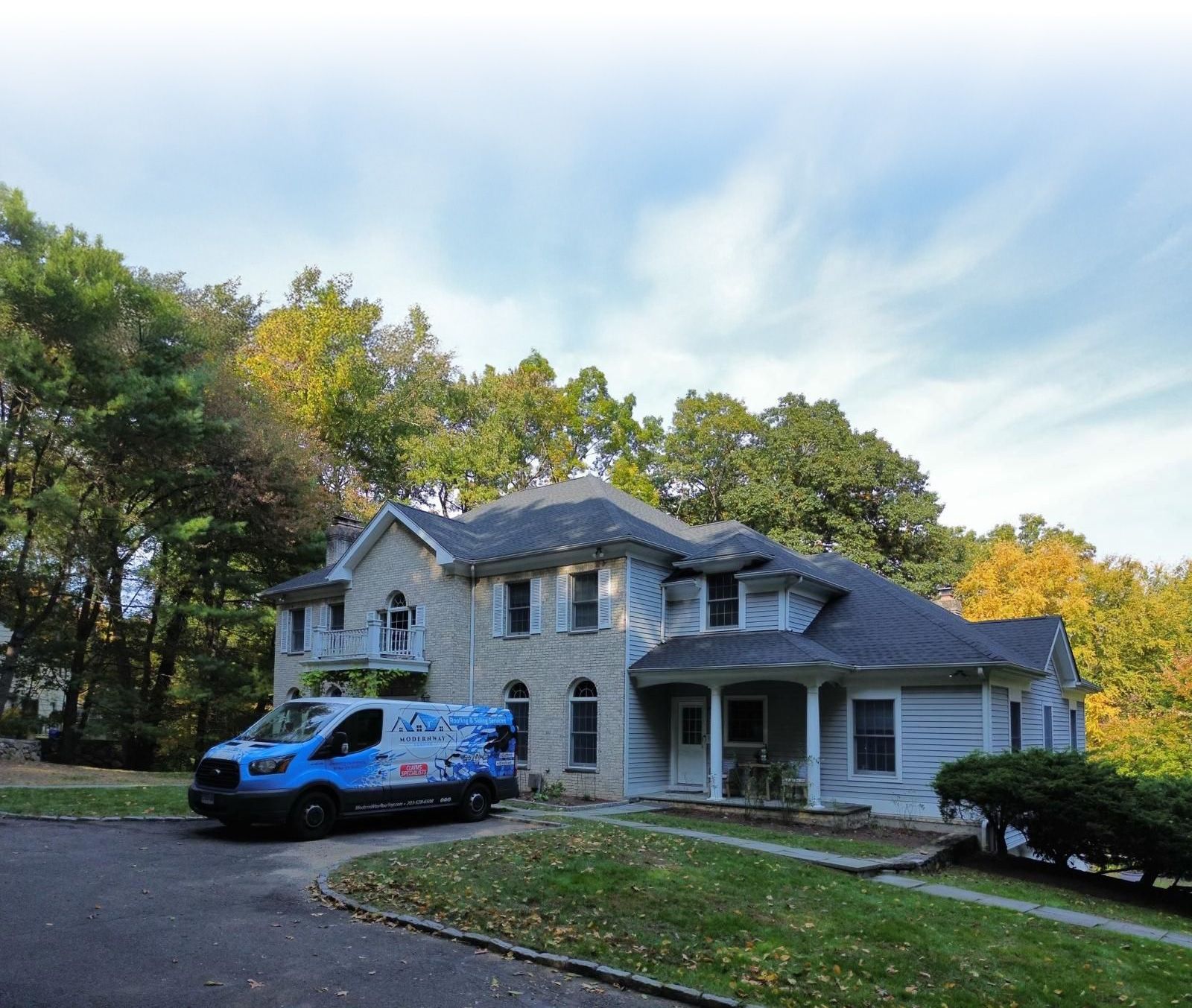 Blue van parked in front of a light blue two-story house with a lawn and trees.