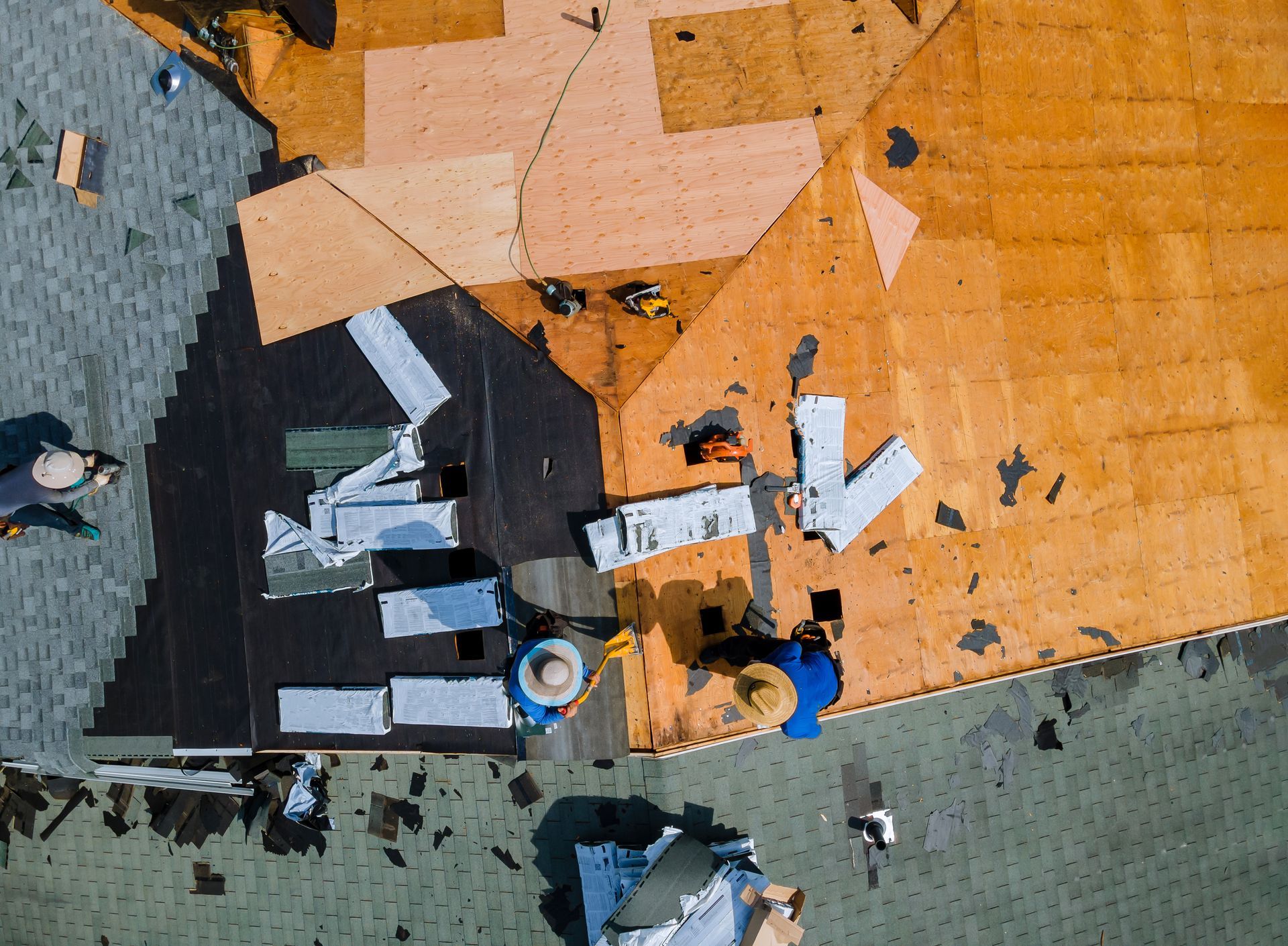 Roofers installing shingles on a house roof; workers in action with tools, wood, and shingles.