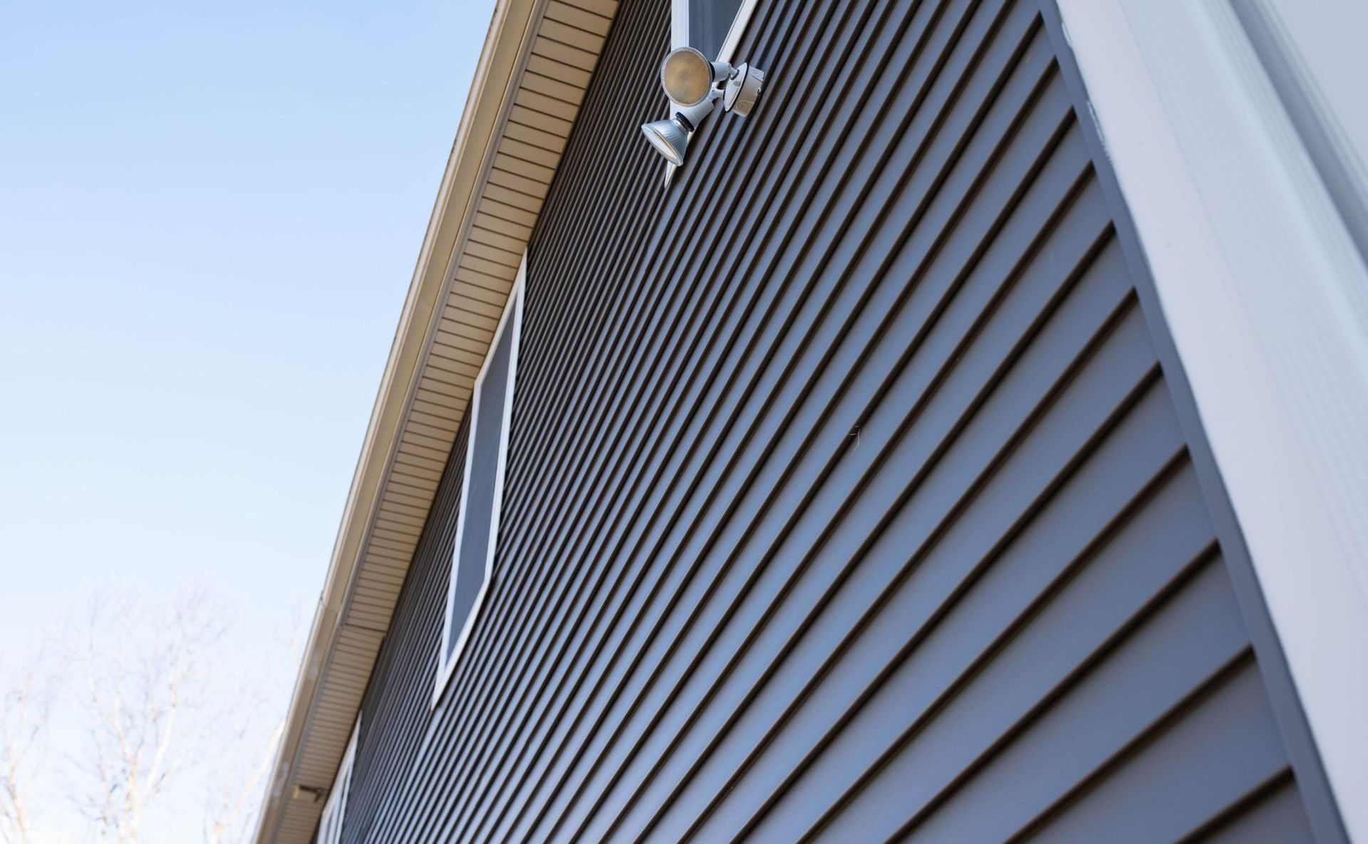 Dark gray siding on a house with white trim, tan soffit, and security camera against a blue sky.