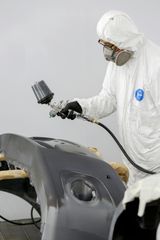 Person in protective suit spray painting a car bumper.
