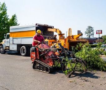 A man is driving a tree chipper next to a truck.