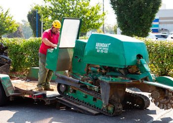 A man is standing next to a green machine on a trailer.