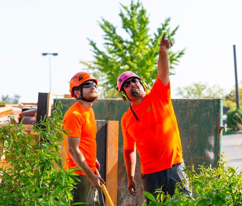 Two men wearing orange shirts and hard hats are standing next to each other.