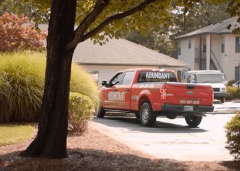 A red truck with the word abundant on the back is parked in front of a house.