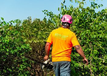 A man wearing an orange shirt and a pink helmet is walking through a forest.