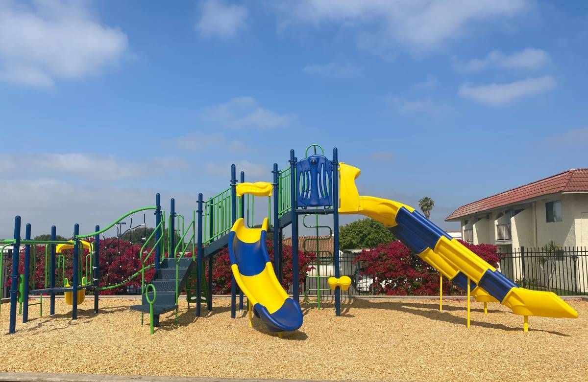 A blue and yellow playground set in a park with a house in the background.