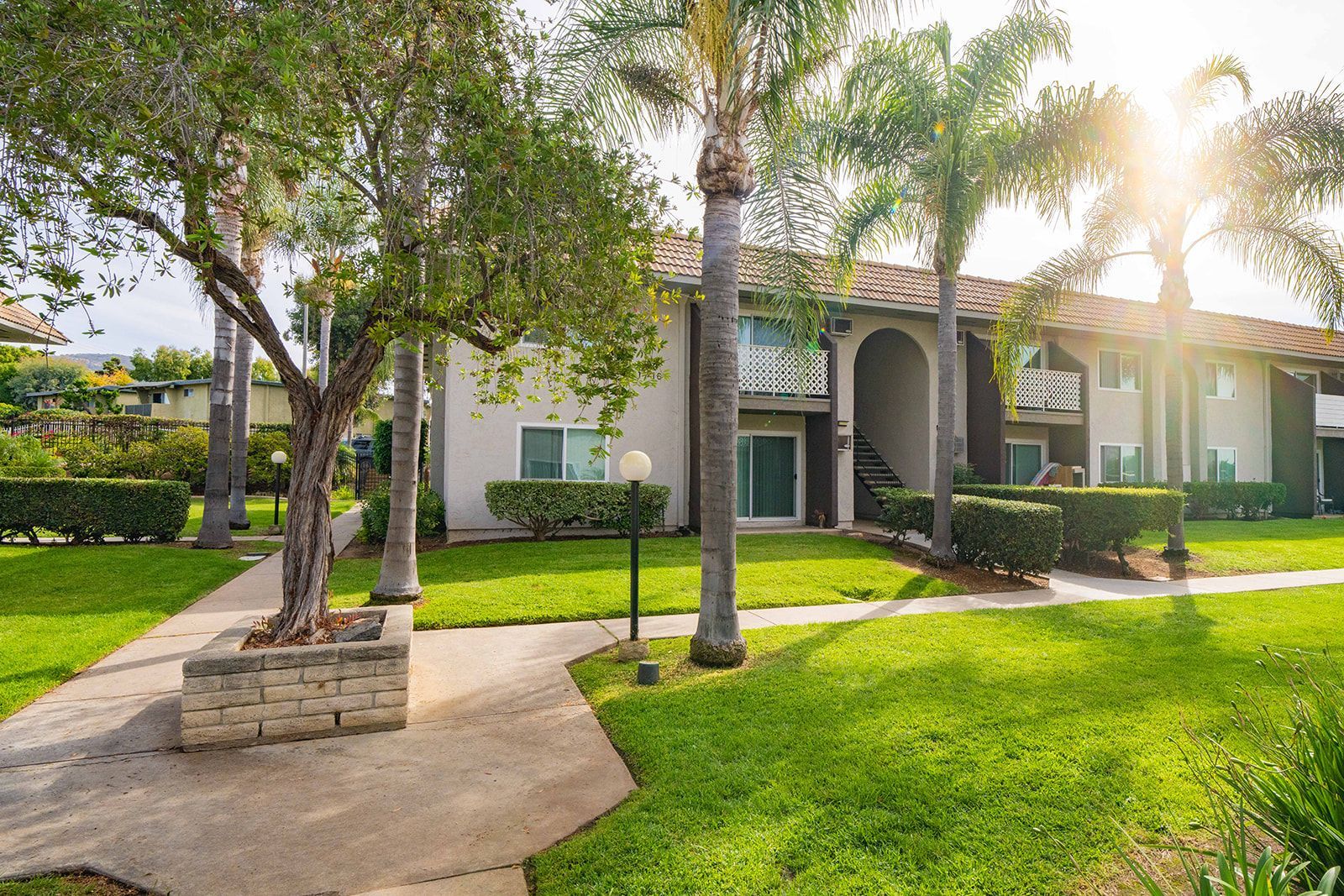 A white apartment building with a lush green lawn and palm trees in front of it.