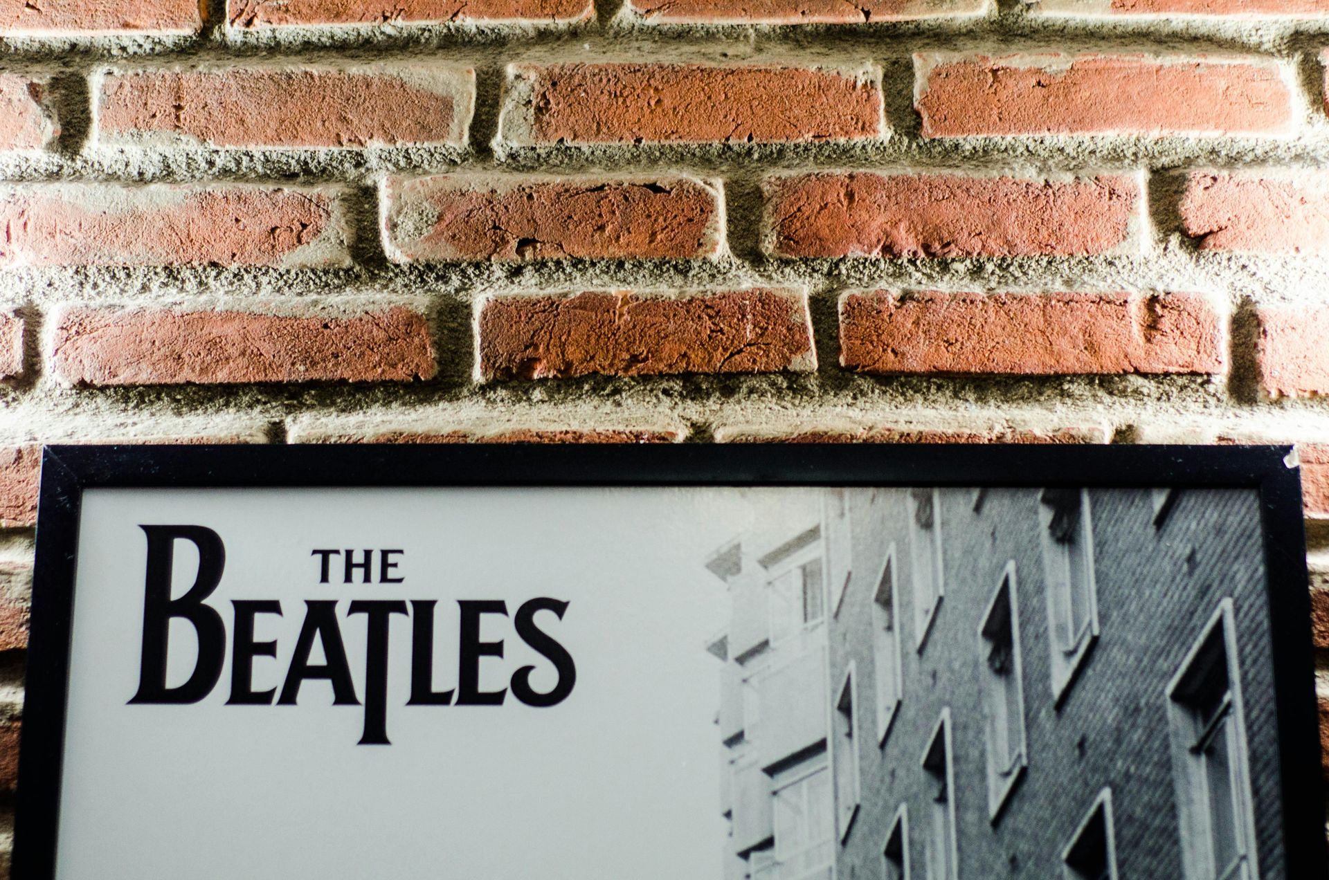 A framed picture of the beatles is hanging on a brick wall.