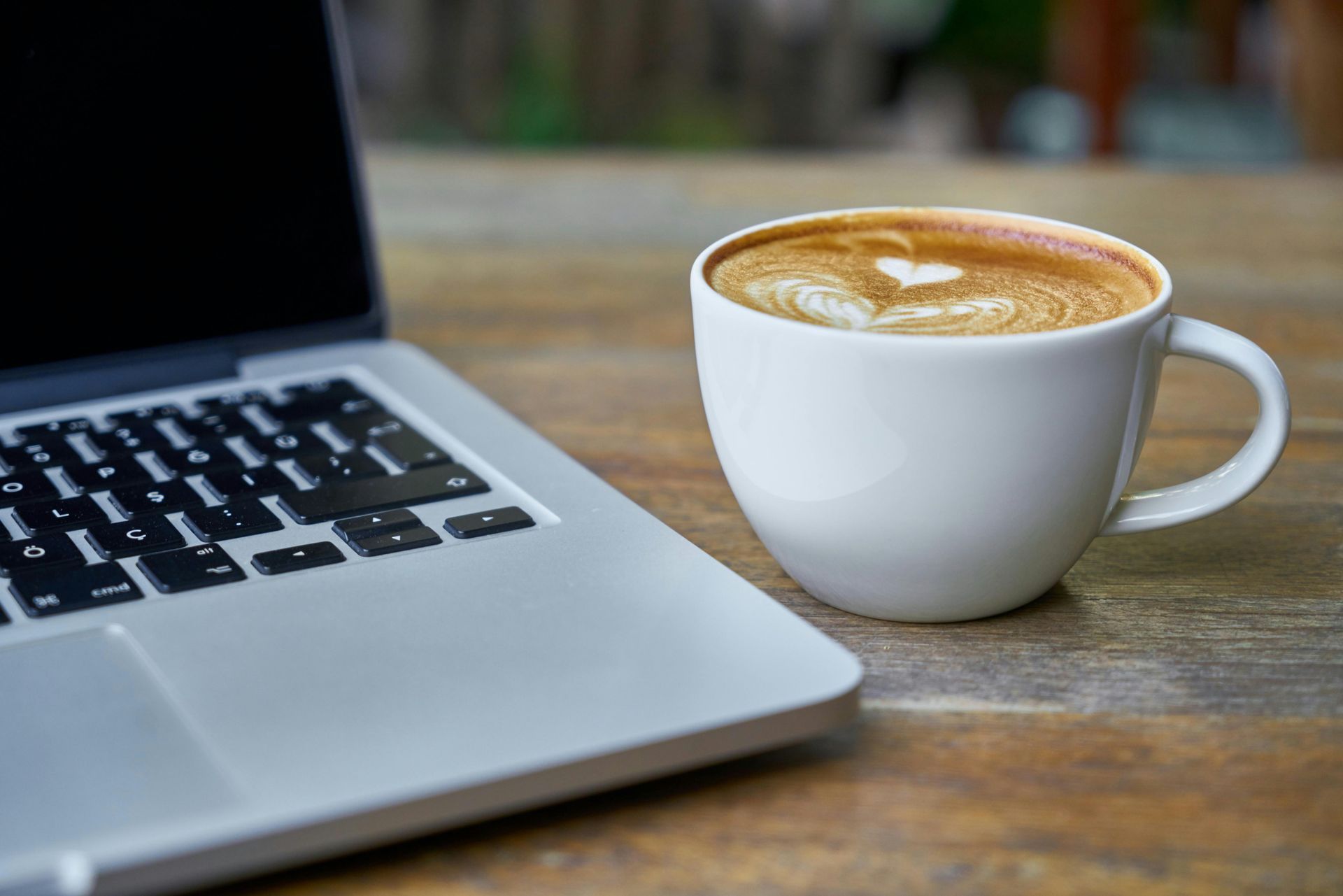 Laptop and coffee cup with latte art on a wooden table.