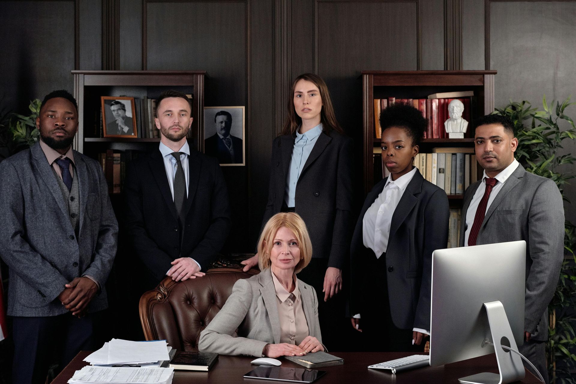 Group of people in suits standing and sitting in a law office, looking at the camera.