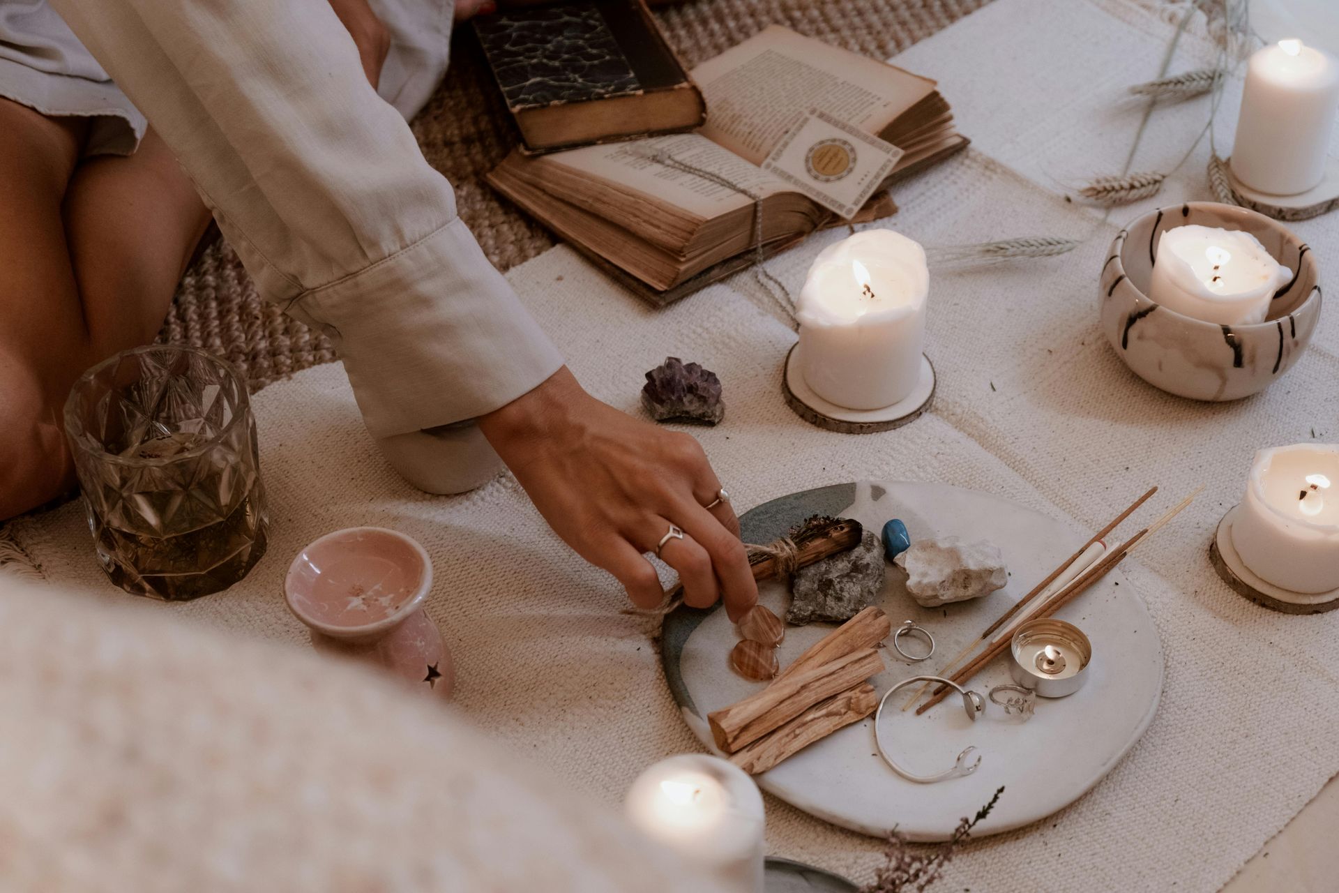 A person is sitting on the floor surrounded by candles and crystals.