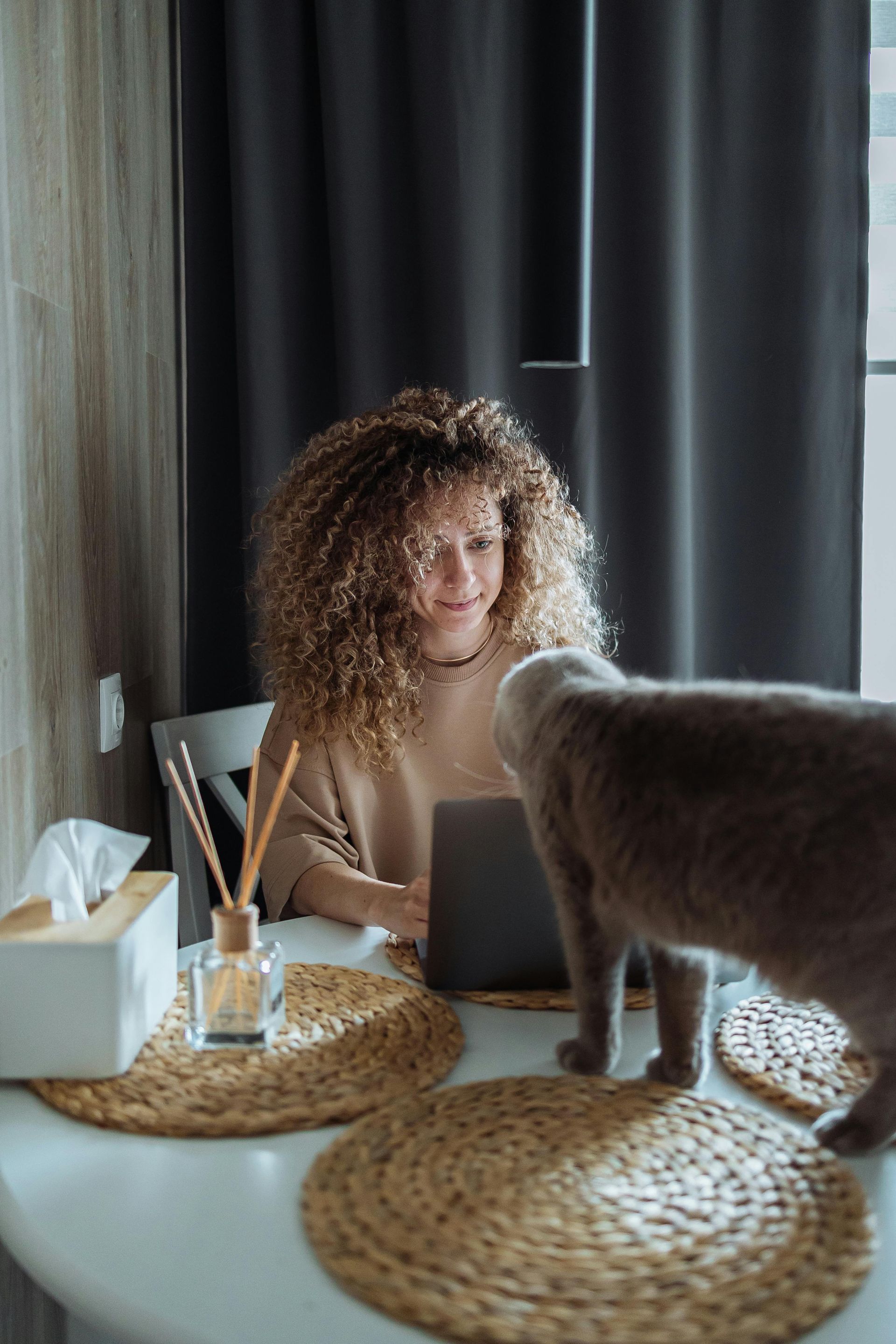 A woman is sitting at a table with a laptop and a cat.