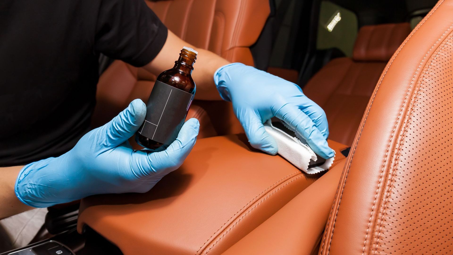 A person wearing blue gloves is cleaning the leather seats of a car.