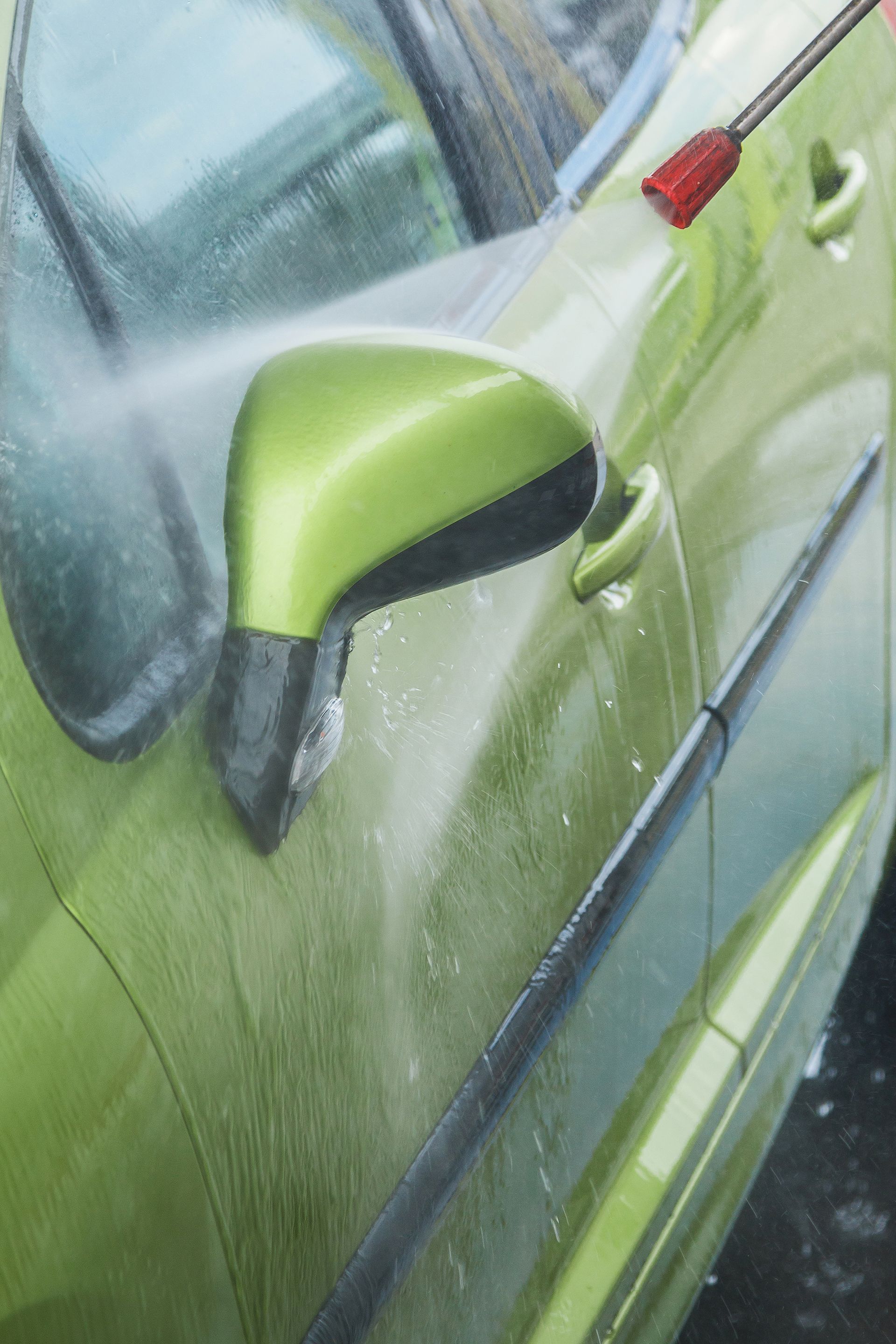 A person is washing a green car with a high pressure washer.