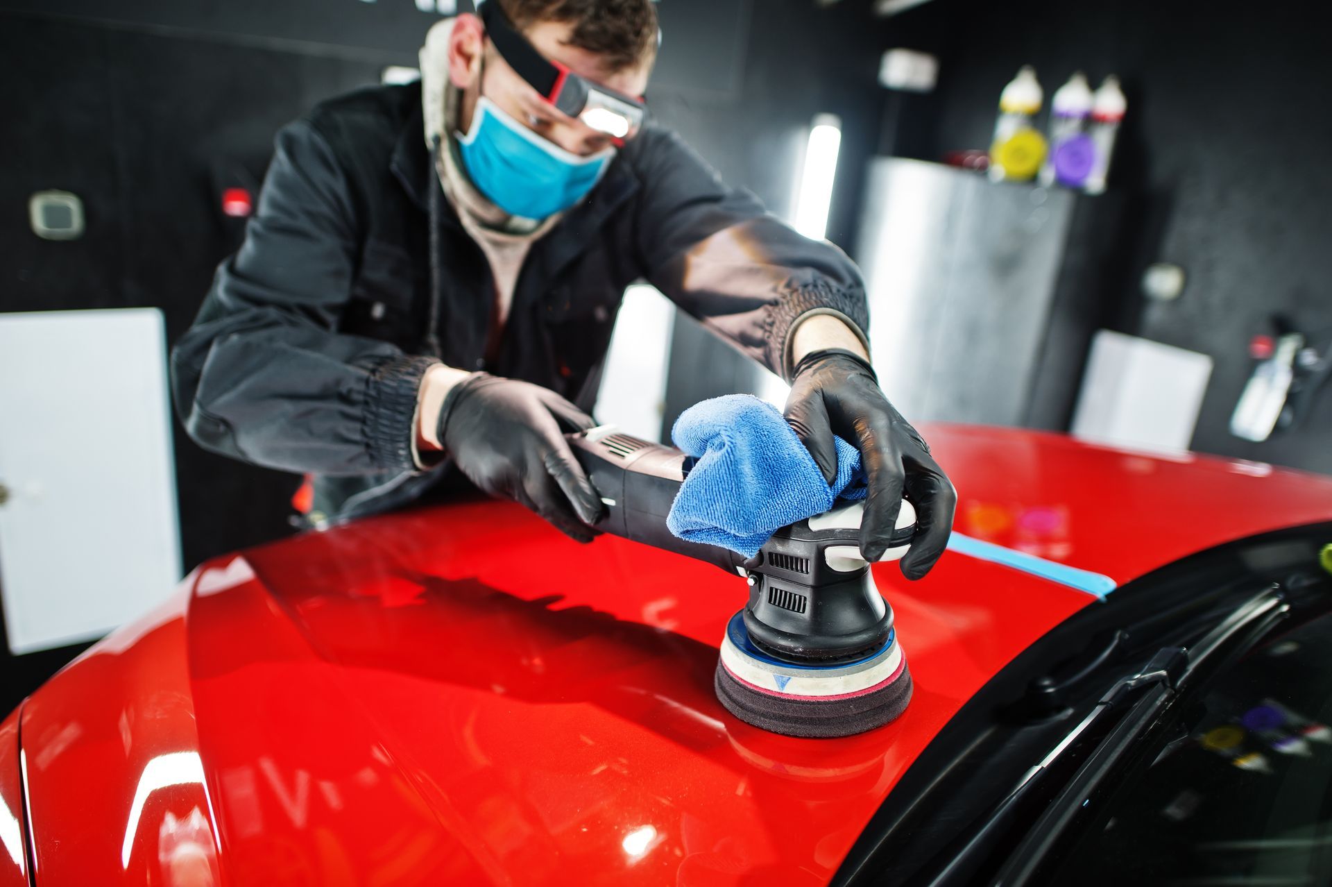 A man wearing a mask and gloves is polishing a red car.