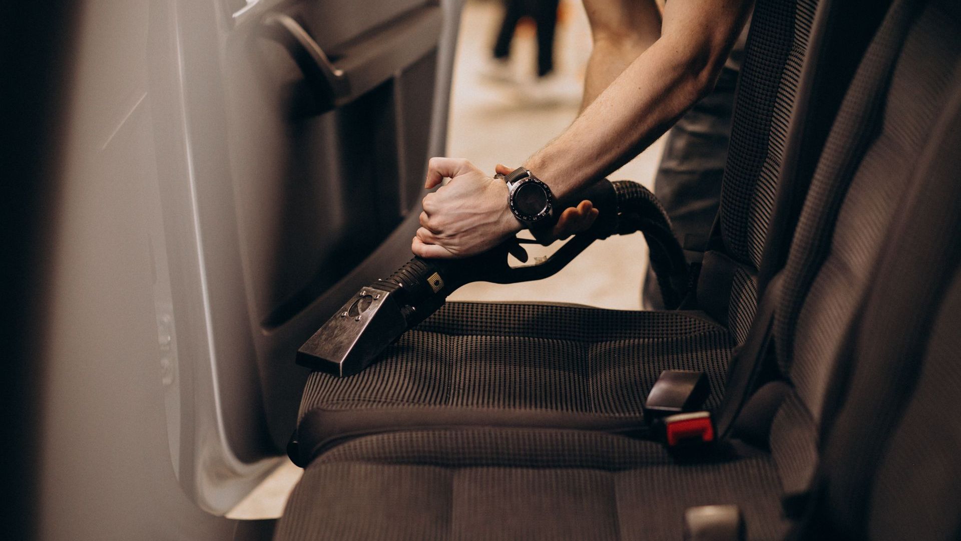 A man is cleaning the seats of a car with a vacuum cleaner.