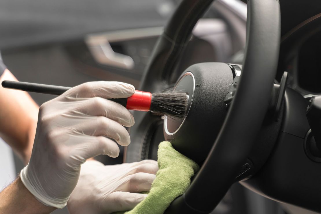A person is cleaning the steering wheel of a car with a brush.