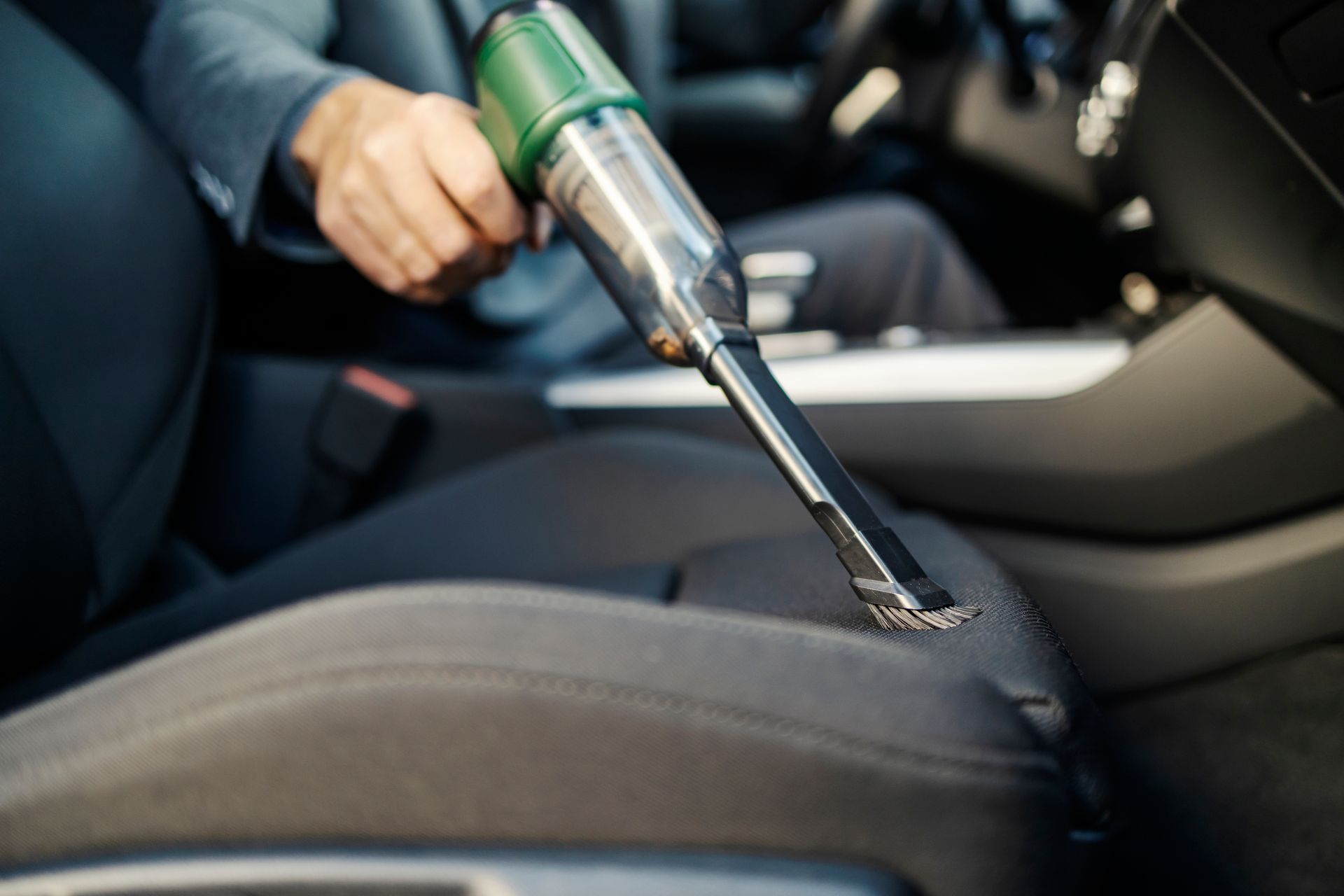 A man is cleaning the seats of a car with a vacuum cleaner.