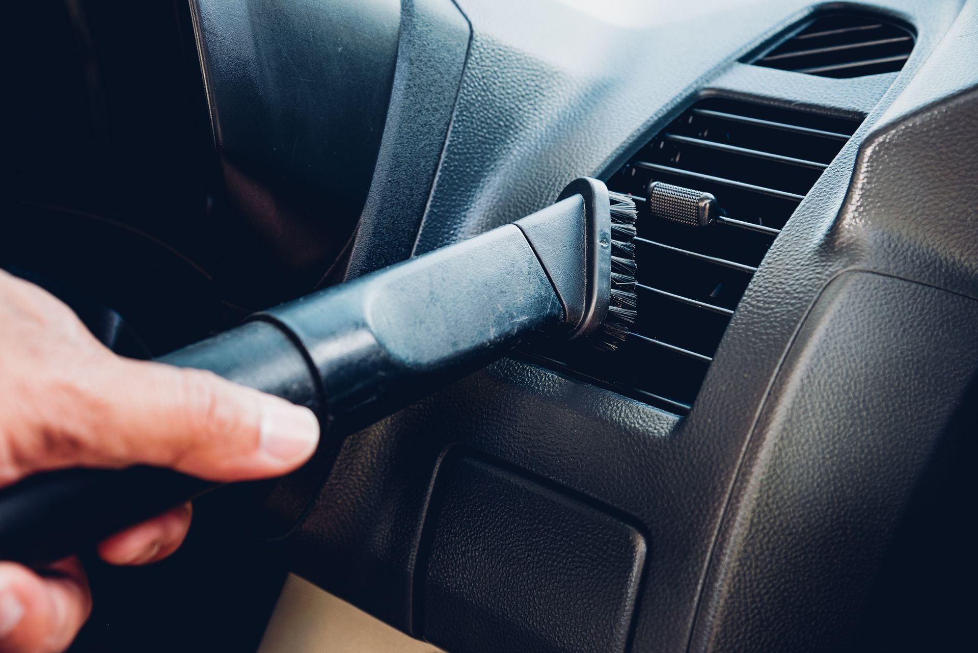 A person is using a vacuum cleaner to clean the air vents of a car.