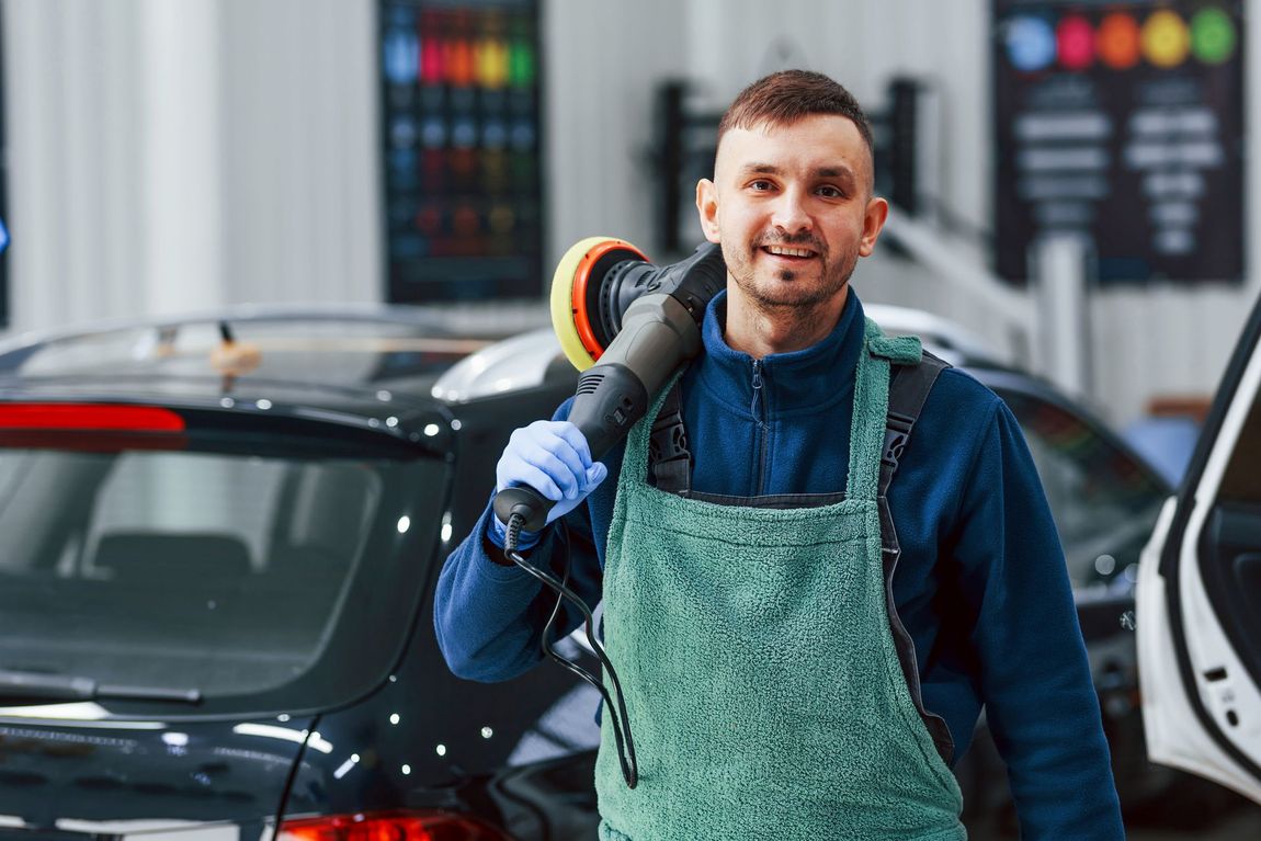 A man is standing in front of a car holding a polisher.