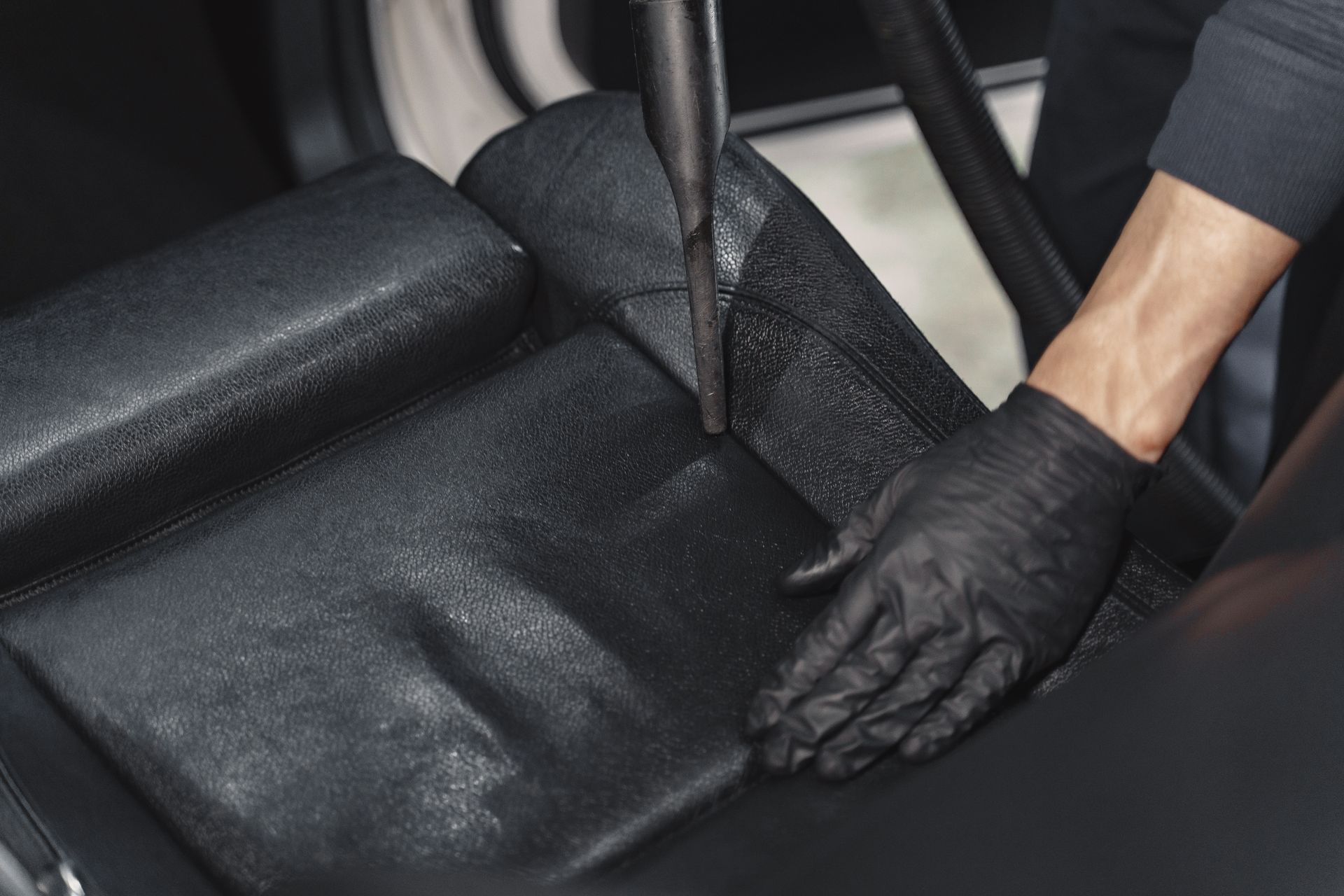 A person wearing black gloves is vacuuming the back seat of a car.