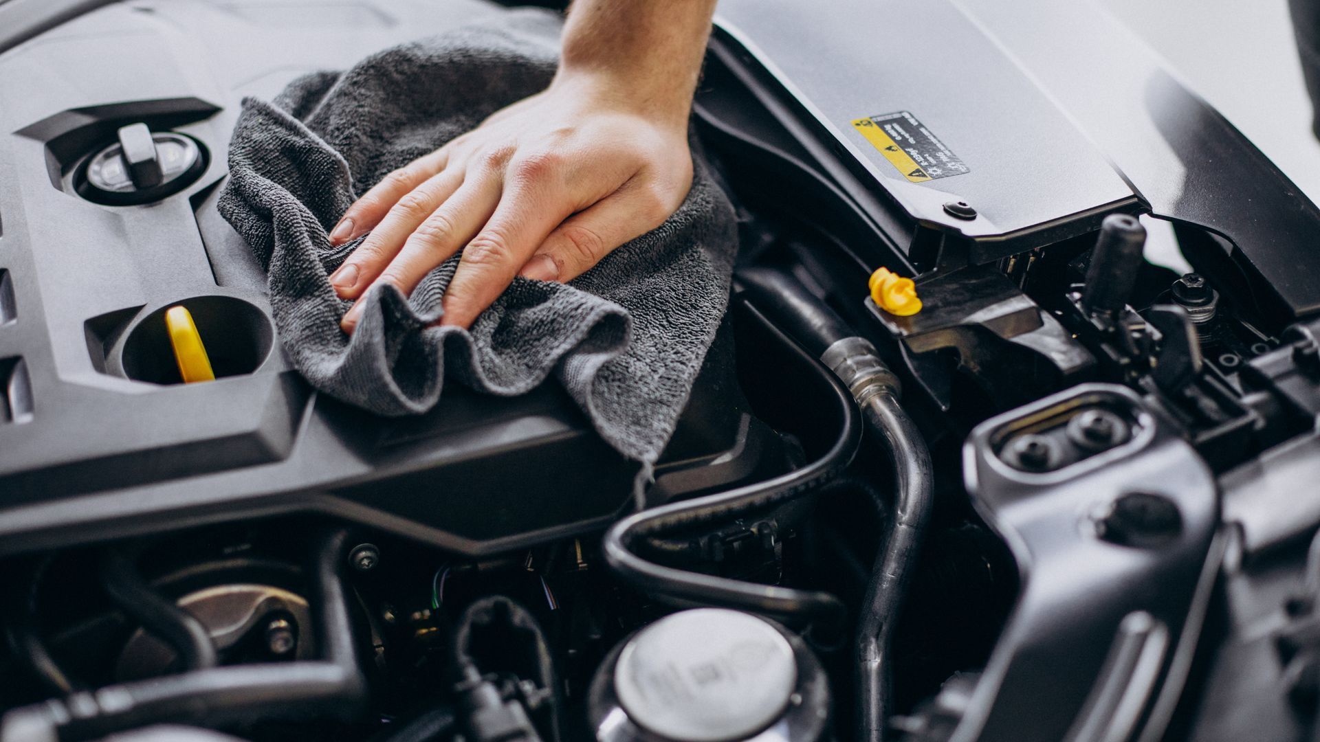 A person is cleaning the engine of a car with a towel.