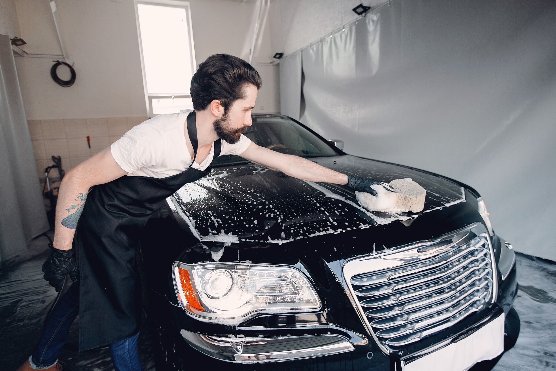 A man is washing a black car with a sponge.