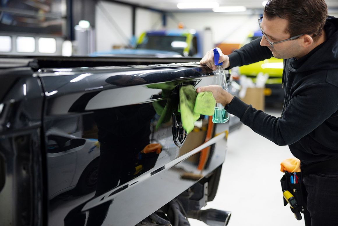 A man is cleaning the side of a car in a garage.