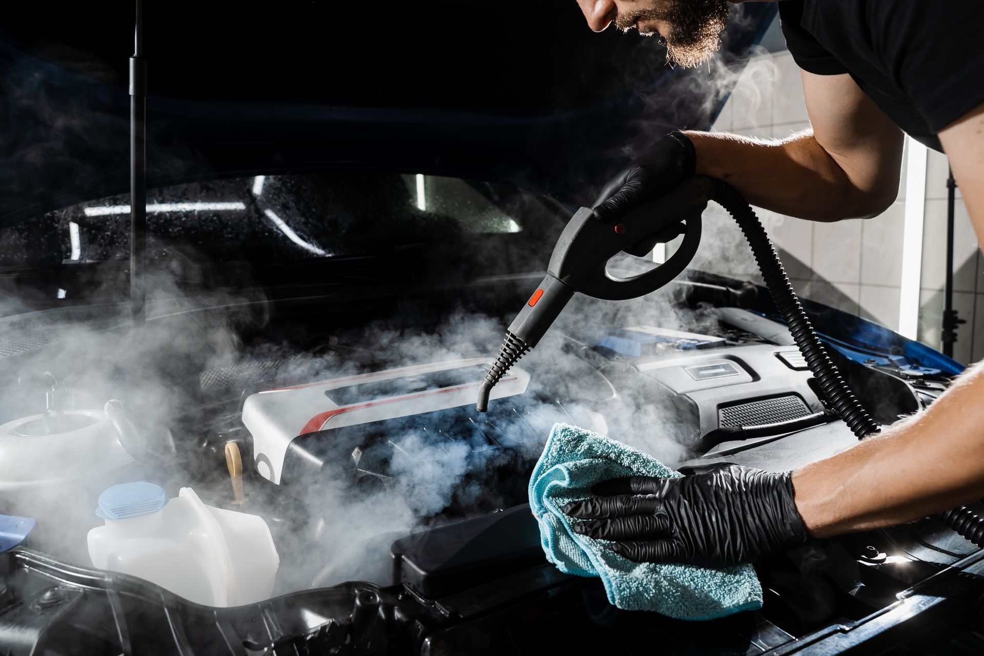 A man is cleaning the engine of a car with a steam cleaner.