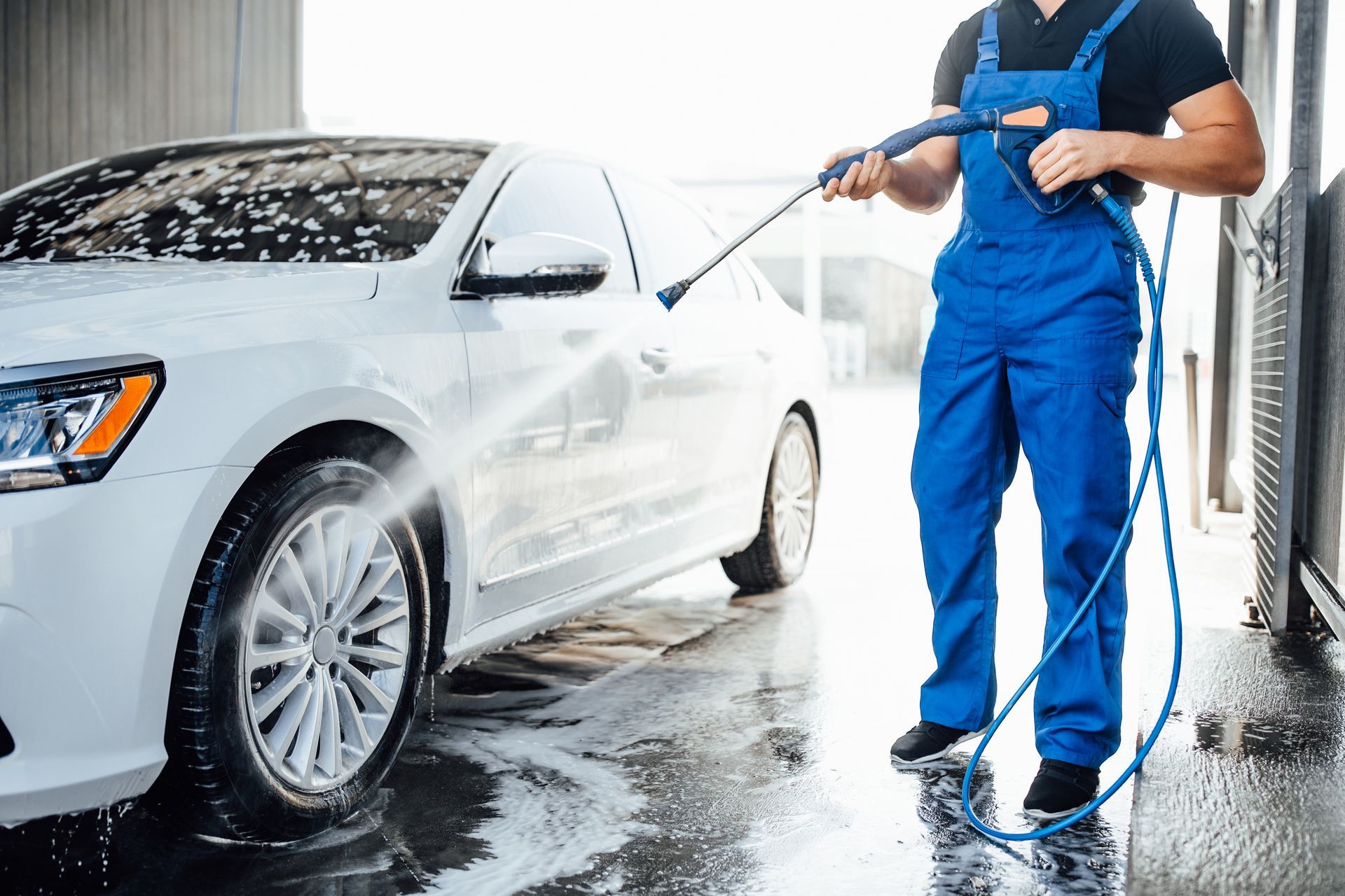 A man is washing a white car with a high pressure washer.