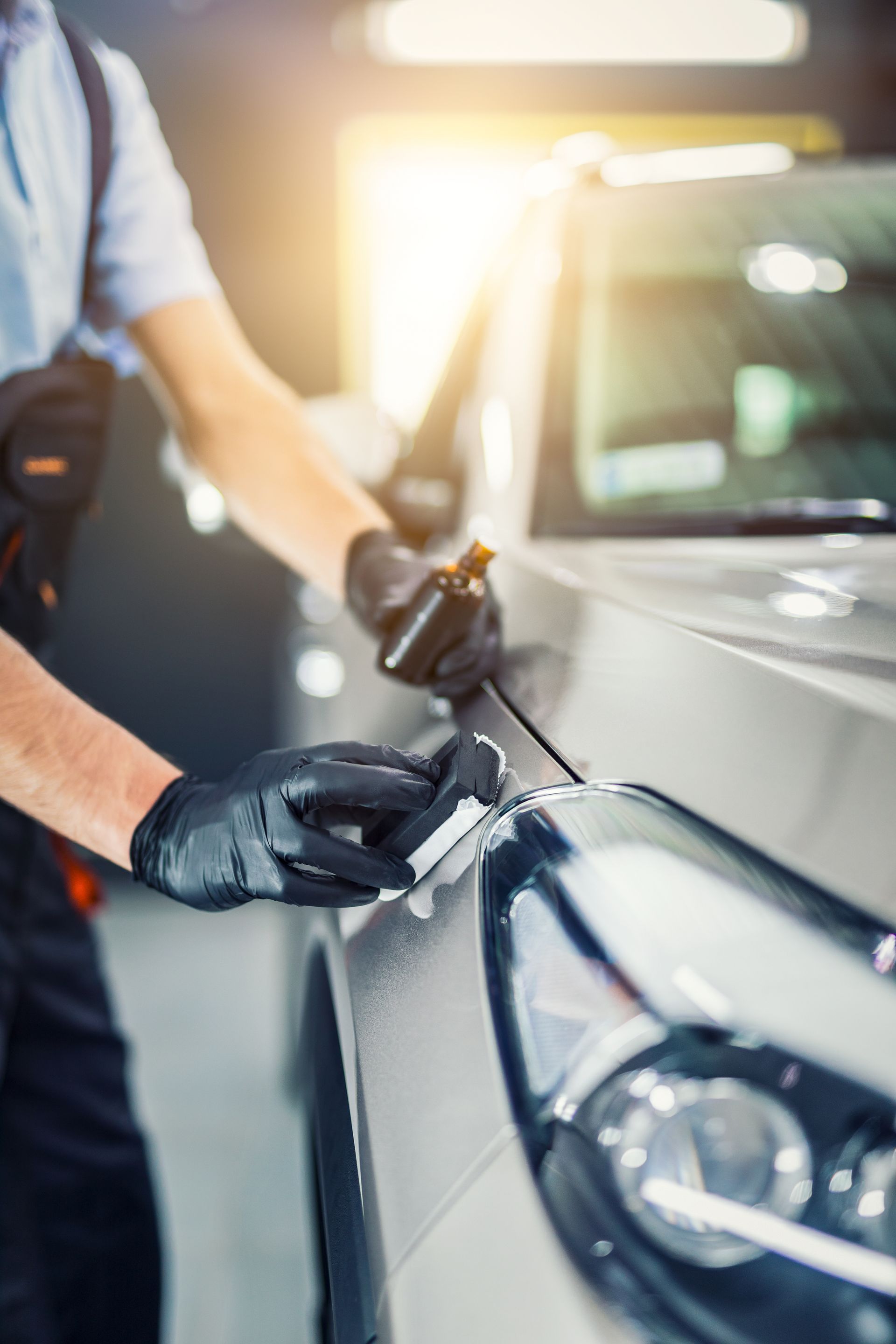 A man is polishing the headlight of a car in a garage.