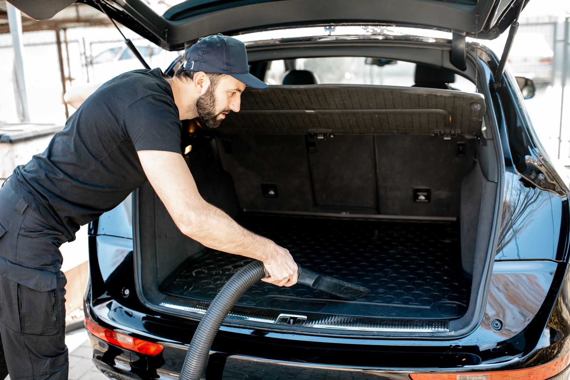 A man is cleaning the trunk of a car with a vacuum cleaner.