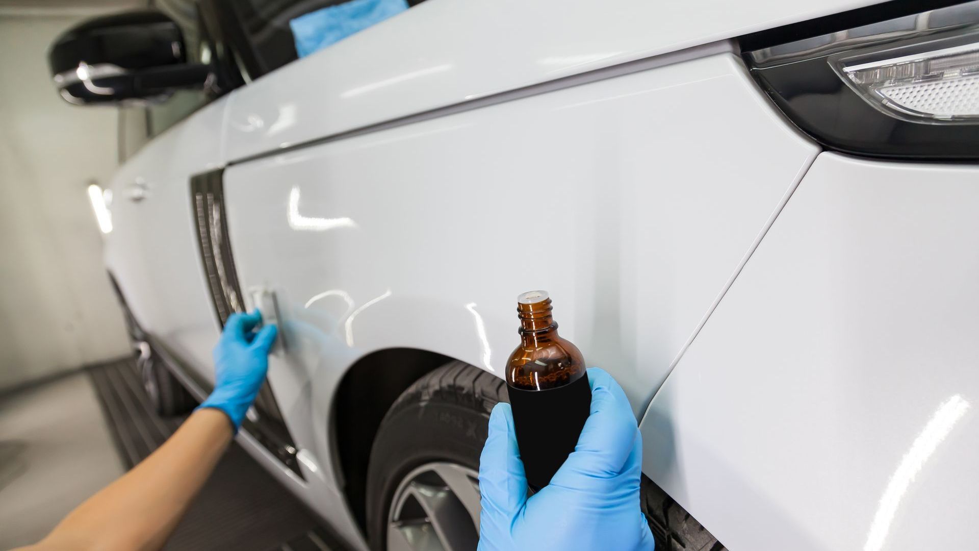 A person is applying a coating to a white car.