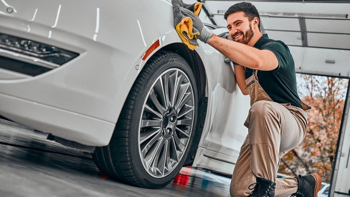 A man in a green jacket is washing a car with a hose.