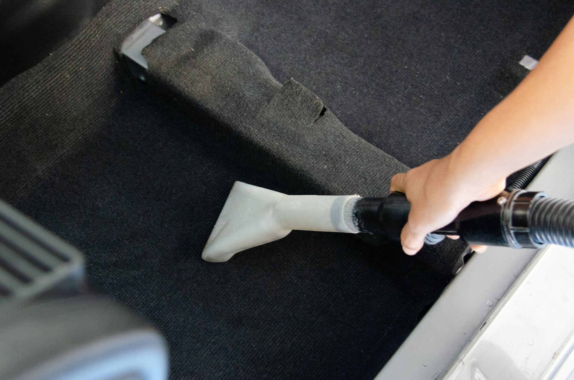 A person is using a vacuum cleaner to clean the carpet in a car
